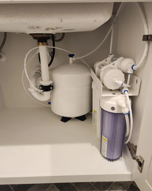 5-stage reverse osmosis system with storage tank under a white kitchen cabinet