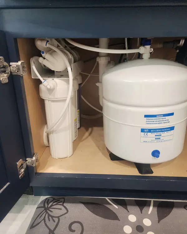 5-stage reverse osmosis system with storage tank under a navy kitchen cabinet
